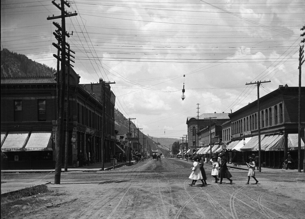 One 5" x 7" b/w glass plate negative of Hyman Avenue and Galena Street at the turn of the century. Some girls are crossing the street on Galena Street. The Aspen Block, Wheeler Opera House, Kobey building and Aspen Drug are pictured. The Carbon Filamant street lights are visible. See also the horse drawn carriage, wagon in the background. 1900-