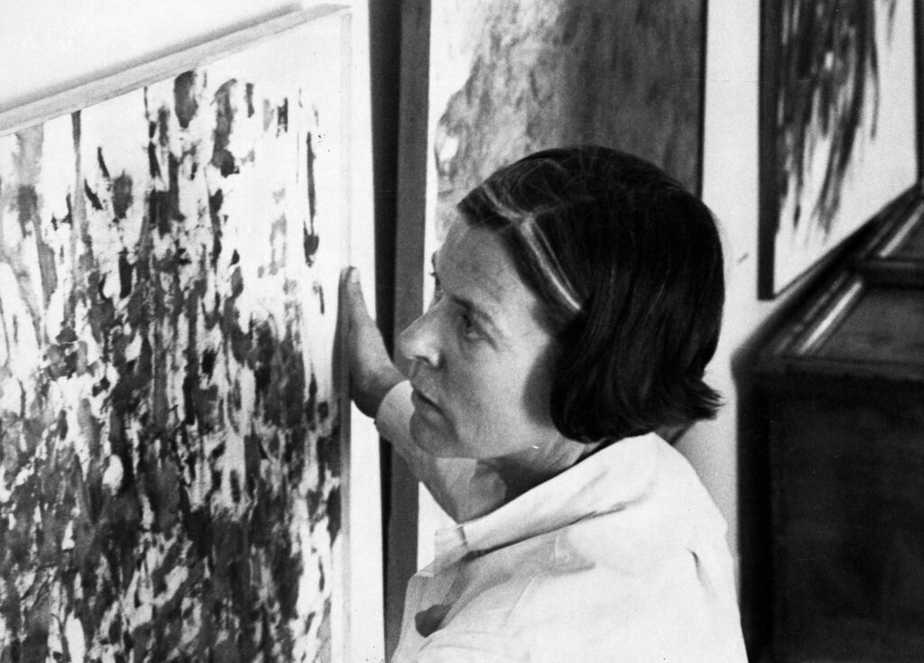 Head shot of Patrician Moore hanging paintings in her gallery